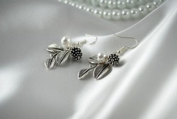 A silver earring with a pearl, leaves and a silver cone lying on the satin 