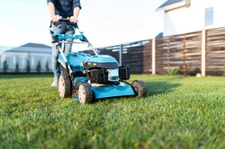 Garden equipment. Gas-push lawn mower on the green grass, male legs on background