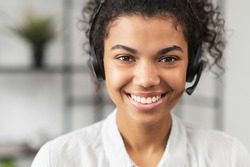 Headshot of friendly African American millennial woman in headset, smiling and working in emergency helpline or in the customer service department as call center operator, helping client with inquiry