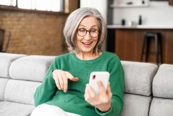 Happy beautiful senior woman is using a smartphone for video calling to family, friends or dating online. Mature elderly lady holds the phone and using app for video communication, online meeting