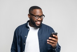 Portrait of cheerful young black guy sending message on mobile phone over white background. Happy African-American man using smartphone, enjoying chatting online, messaging in social networks