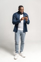 Joyful and carefree African-American man using smartphone isolated on grey, black guy spends leisure in social networks, chatting online, shopping, using new mobile app, full length, vertical