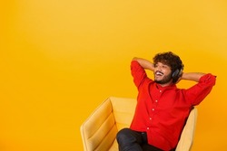Studio portrait of relaxed cheerful indian man wearing and holding wireless headphones isolated on orange wall, enjoying listening to favorite music soundtrack, wellbeing. Meditation concept