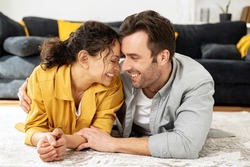 Love and bonding. Serene and carefree couple in love bonding to each other and smiling. Middle-aged handsome man and charming woman lying down in embrace on the floor in living room