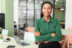 Successful young african-american female entrepreneur, small business owner, female office employee, black businesswoman wearing green casual shirt stands in confident pose with arms crossed