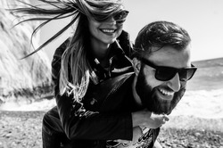 Black&white photo of happy couple in the leather jackets running on the beach