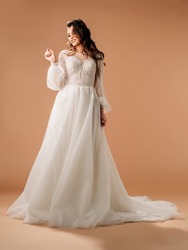Young brunette bride in elegant white lace wedding dress with long sleeves and lush tulle skirt, big train. Full-length portrait of happy smiling bride in studio. Bridal fashion. Wedding inspiration