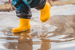 The feet of a child in rubber boots stomp through puddles