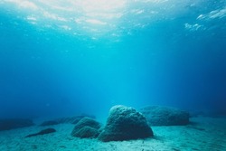 Rocks on sand at bottom of ocean floor in blue clear sea