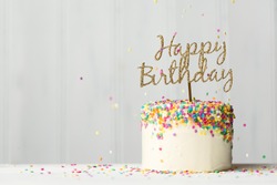 Colorful birthday cake with golden happy birthday banner and falling sprinkles