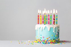 Birthday cake with white drip icing, sprinkles and colorful birthday candles