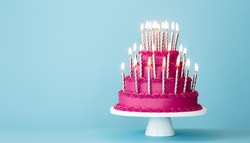 Extravagant pink tiered birthday cake with lots of gold birthday candles against a blue background