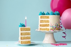 Birthday cake with layers and turquoise frosting, slice removed and one pink birthday candle