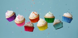 Banner with row of tumbling colorful rainbow cupcakes with falling sugar sprinkles