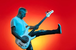 Screaming hipster man play white bass guitar in neon lights. Rock music concept