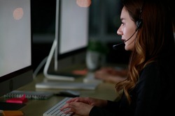 Young Asian lady customer services care operators working night shift in call center for helping assistance client in workplace at night time. Night shift Call center business operator 24hours concept