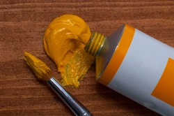 Tube of yellow oil paint and brush on wooden background