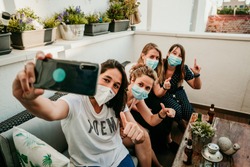 Group of young girlfriends meeting after the quarantine caused by the covid19. Taking precaution with surgical masks and taking photos together with a smartphone.