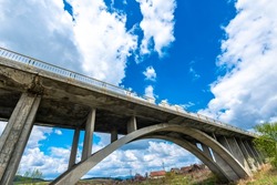 Concrete bridge in arch shape over Olt river in Transylvania, Romania, blue sky with white clouds background.