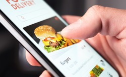Food delivery app order with phone. Online mobile service for take away burger and pizza. Hungry man reading restaurant menu, website and reviews with smartphone. Takeout or fast courier deliver.