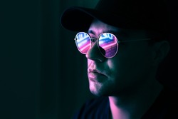 Neon reflection in glasses. Man in fluorescent light from city led sign. Mysterious cool model in futuristic cyberpunk portrait. Guy in sunglasses. Techno rave party disco art. Dark black background.