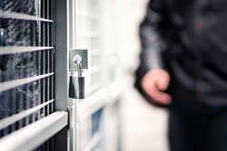 Burglar or thief and storage with lock in basement of condo apartment building. Suspicious man, intruder and criminal. Door with padlock for security and protection. Cage locker in cellar or garage.