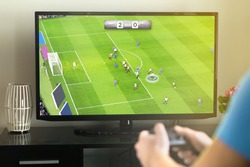 Young man hanging out and playing imaginary soccer or football video game with console and tv. Holding controller in hand. Fun freetime activity.