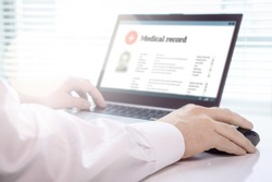 Doctor using laptop and electronic medical record (EMR) system. Digital database of patient's health care and personal information on computer screen. Hand on mouse and typing with keyboard.