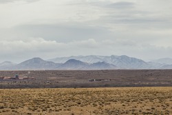 Snow covered mountains and open plains of a wide open desert vista landscape on overcast day in rural New Mexico