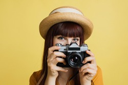 Hobby, taking photos, travel concept. Gorgeous young woman in hat, photographer amateur, smiling and taking picture on old vintage camera, on colorful yellow studio background.