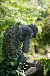 Weeping Sculpture With Overgrowing Ivy Leaves Growing On The Back. Head Bowed And In Hands Prayed. Leipzig, Germany