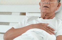 Sad senior man lying on the hospital bed and with a nasal breathing tube for treatment respiratory. Concept of Health care for the elderly, quarantine coronavirus (COVID-19)