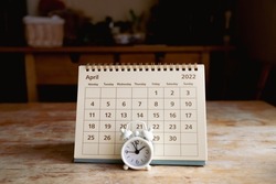April 2022 calendar and little vintage white alarm clock on a wooden table