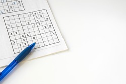 sudoku puzzle book with blue pen, against white background. space for text