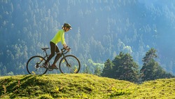 A young smiling woman on a cyclocross bike rides against the background of a green forest on a sunlit meadow