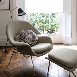 Comfortable light green armchair in cosy setting with cushion on dark wood floor in front of tall window. 