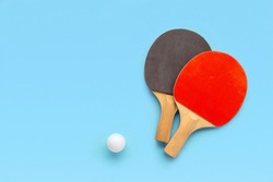 Red and black rackets for table tennis with white ball on blue background. Ping pong sports equipment in minimal style. Flat lay, top view, copy space