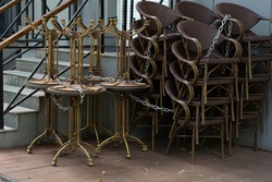 Stack of outdoor tables and chairs of cafe linked by metal chain, which closed during pandemic of COVID-19 virus. COVID-19 restrictions on public cafe.