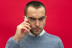 Portrait, attractive, overwrought guy, man talking on phone, looking at the camera, front view, bright red background, close up