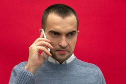 Portrait, attractive, overwrought guy, man talking on phone, looks back to side, front view, bright red background, close up