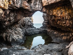 Beautiful landscape photograph of a hidden gem of a natural rock bridge arching over a pool of water on the island of Lokrum in Croatia in Europe with a view out to the Adriatic Sea.