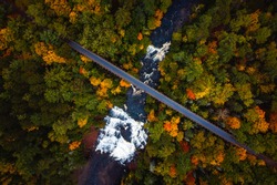 Beautiful look down travel aerial photograph of the abandoned railroad bridge crossing the Ontonagon River and scenic Agate Falls waterfall below surrounded by forest of evergreen and deciduous trees.