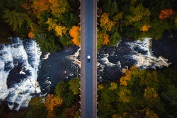 Beautiful autumn look down travel aerial of a man laying down on the abandoned railroad bridge crossing the Ontonagon River and scenic Agate Falls waterfall below surrounded by forest of trees.