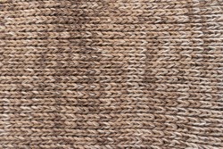 Knitted background. Knitted wallpaper. Beige knitted fabric. Knitted texture. Soft material. Brown, beige and white handmade sweater close up photo. Cozy background. Knitwear detail. Woolen cloth.