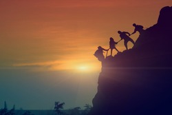 Asian young couple silhouette climbing the mountain hiking and teamwork concept, sunset background