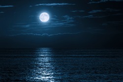 This large full blue moon rises brightly over the cloud bank in this calm ocean creating sparkles accross the waves in this beautiful tranquil scene. 