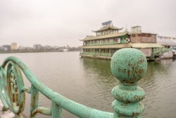 In Hanoi, Vietnam, balustrade up close, with abandoned dinner cruise ship beyond, in a beautiful waterscape on West Lake (Tay Ho). Very shallow focus for effect on cracks on left side.