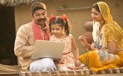 Rural Indian family using laptop on traditional bed at village