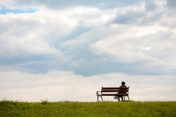 Line horizon and earth on the background of beautiful clouds. One woman sits on a bench and looks at the sea. Horizontal frame. Color photography