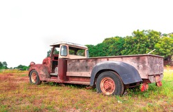 Old truck is being reclaimed by nature in a meadow along with an old tractor wheel in Thailand.